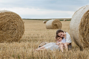 Naklejka na ściany i meble Young mother and her son are hugging near straw bales in a field. A happy family. Mother's day