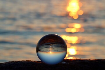 Crystal ball on rocky beach on a granite boulder, sunset reflecting in the sea, background blurred