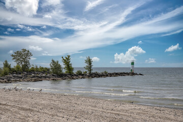 View from beach toward water and small rocky peninsula with lighthouse, blue sky and clouds, nobody