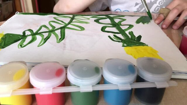 kid drawing dandelion flowers with gouache paints in album.