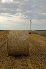 a modern village, hay bales on the field after the harvest on the background of wind turbine, windmill