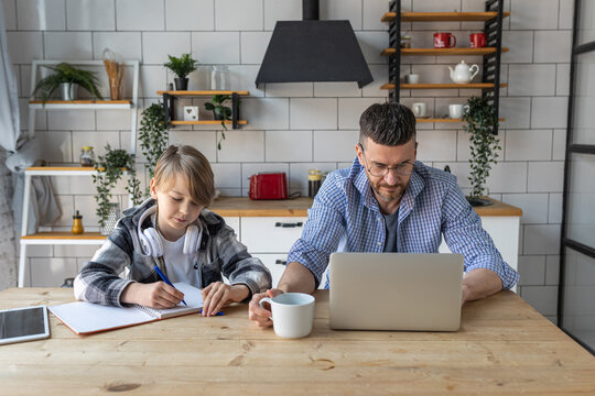 Father helping his teenage son with homework while working from home in the kitchen. Concept of parenthood, fatherhood, spending quality time together. Using technology, gadgets, devices for learning