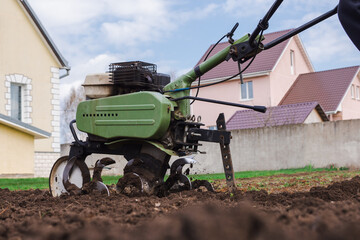 motor cultivator or tiller tractor cultivates the ground soil in the garden close up. Modern...
