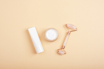 Rose quartz crystal facial roller, cream jar and tube on neutral beige background. Natural cosmetics, skin care concept. Top view, flat lay, mockup