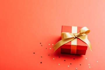 Red gift in a box with golden ribbon and confetti on red background. Christmas concept. Top view, copy space