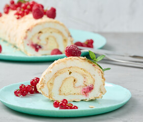 Baked meringue roll with red berries on a round plate, white background