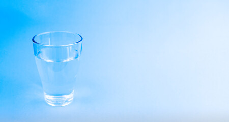 A glass of water on a blue background. Copy space.