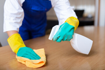 Image of gloved woman's hands cleaning an office desk with a rag and detergents. Close-up image