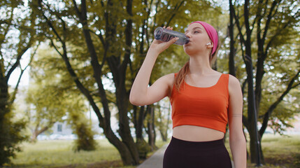 Athletic fit sport runner girl drinking water from bottle after training exercising. Workout cardio in park at morning. Young slim woman jogger enjoy healthy lifestyle. Active sportswoman activities