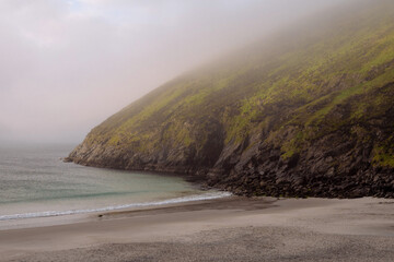 Keem bay and beach in the morning. Low clouds and fog over mountain and water. Calm and moody nature scene. Nobody. Popular travel area. Ireland.
