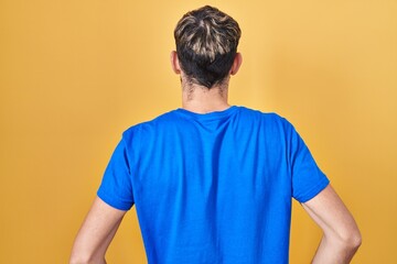 Hispanic man with beard standing over yellow background standing backwards looking away with arms on body