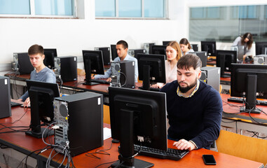 Group of positive young people of different ages learning to use computers in classroom
