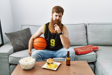 Caucasian man with long beard holding basketball ball cheering tv game looking confident at the camera smiling with crossed arms and hand raised on chin. thinking positive.