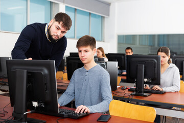 Fototapeta na wymiar adult teacher helping young male student in computer class in university