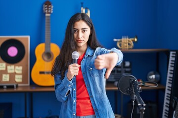 Fototapeta na wymiar Young teenager girl singing song using microphone with angry face, negative sign showing dislike with thumbs down, rejection concept