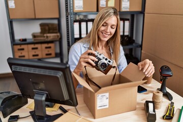 Young blonde woman ecommerce business worker packing vintage camera on order package at office