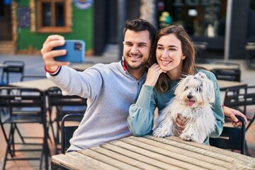 Man and woman holding dog making selfie by the smartphone at coffee shop terrace