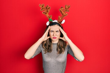 Young hispanic girl wearing deer christmas hat suffering from headache desperate and stressed...