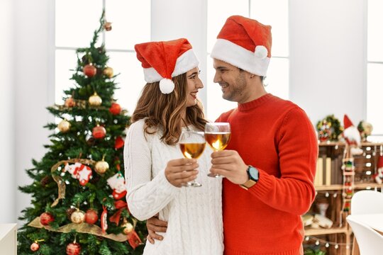Young hispanic couple wearing christmas hat toasting with champagne at home.