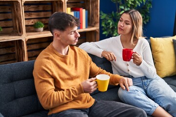 Young man and woman couple drinking coffee sitting on sofa at home