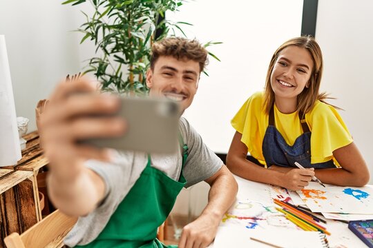 Young hispanic artist couple smiling happy making selfie by the smartphone at art studio.