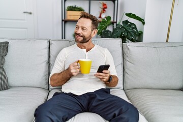 Middle age hispanic man using smartphone drinking coffee at home