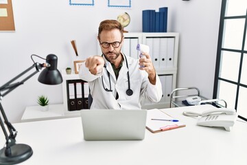 Middle age doctor man holding thermometer at the clinic pointing with finger to the camera and to you, confident gesture looking serious