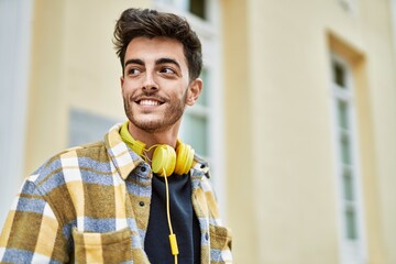 Handsome hispanic man smiling happy and confident at the city wearing headphones with modern style