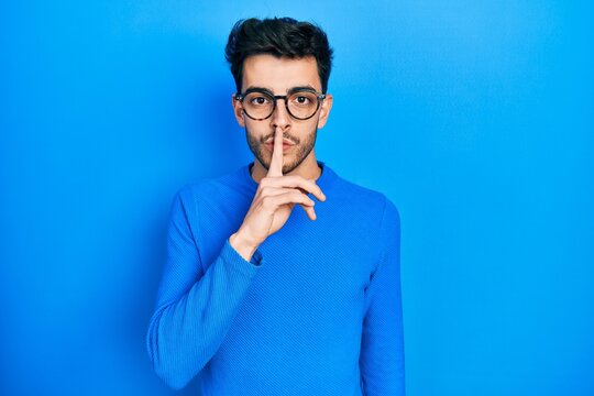 Young hispanic man wearing casual clothes and glasses asking to be quiet with finger on lips. silence and secret concept.