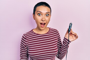 Beautiful hispanic woman with short hair holding usb charger adapter for the car scared and amazed...