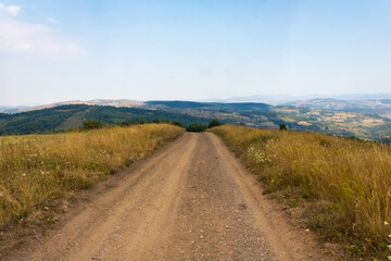 Dry grass field with dirt road and mountains in the distance, Zlatar mountain in Serbia