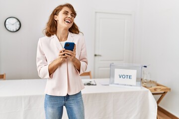 Young caucasian voter woman smiling happy using smartphone at electoral college.