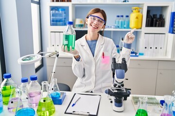 Young brunette woman working at scientist laboratory smiling happy pointing with hand and finger to the side