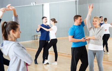 Smiling middle aged woman practicing bachata movements in dance studio for adults