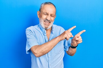 Fototapeta premium Handsome senior man with beard wearing casual blue shirt smiling and looking at the camera pointing with two hands and fingers to the side.