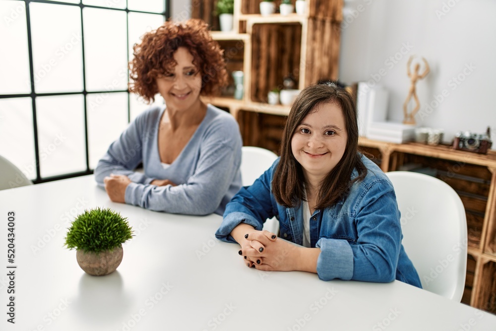 Wall mural mature mother and down syndrome daughter sitting on the table at home