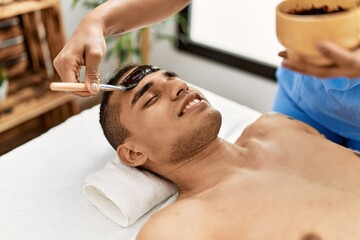 Obraz na płótnie Canvas Latin man smiling happy reciving facial treatment at beauty center.