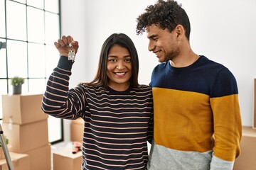 Young latin couple smiling happy and hugging holding key of new home.