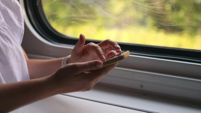 Close-up of girl's hands using smartphone during trip by public train. Female passenger browsing internet while sitting in train, using new apps and functions. Mobile phone navigation and travel