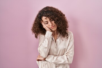 Hispanic woman with curly hair standing over pink background thinking looking tired and bored with depression problems with crossed arms.