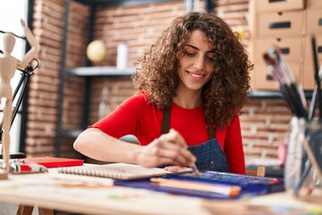 Young hispanic woman artist smiling confident drawing on notebook at art studio