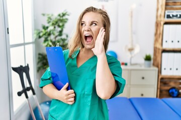 Young caucasian woman working at pain recovery clinic shouting and screaming loud to side with hand on mouth. communication concept.