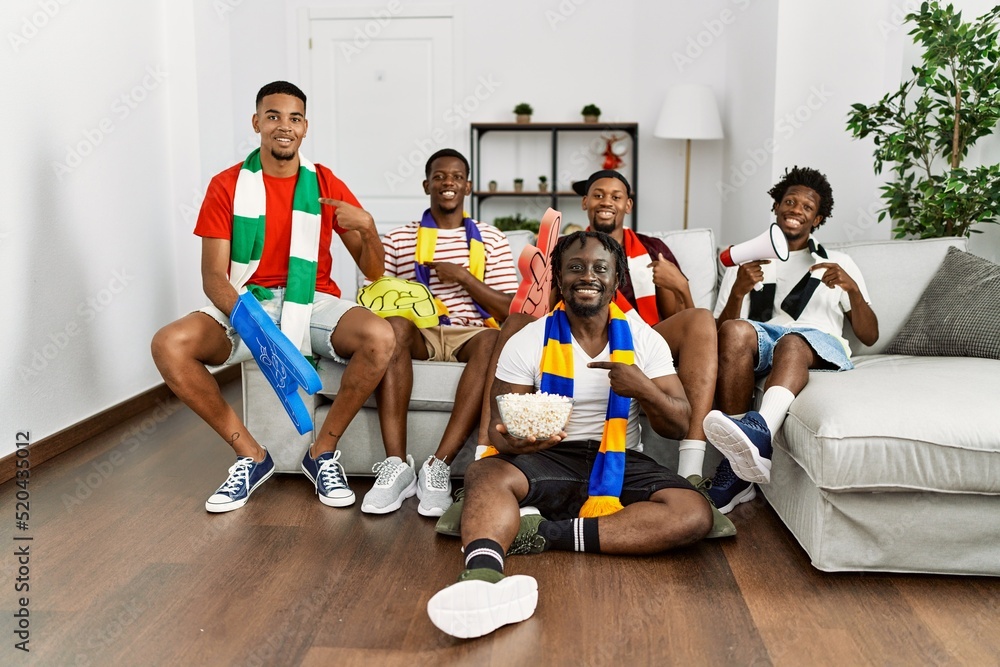 Wall mural young african men wearing team scarf cheering football game smiling happy pointing with hand and fin