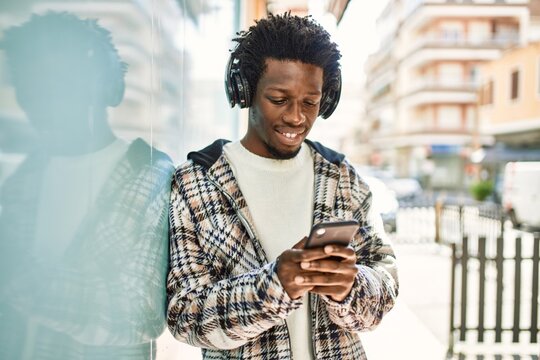 Handsome black man with afro hair wearing headphones and listening to music using smartphone