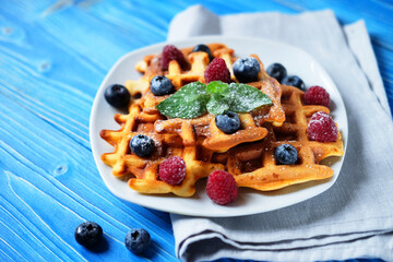 Waffles with blueberries and raspberries for breakfast over blue wooden table.