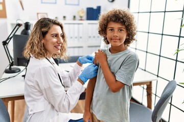 Fototapeta premium Mother and son wearing doctor uniform putting band aid on child arm at clinic