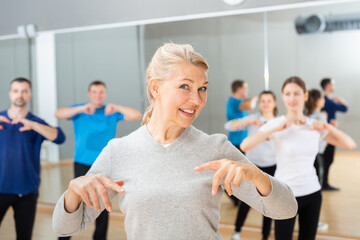 Smiling mature female doing dance workout during group classe in fitness center