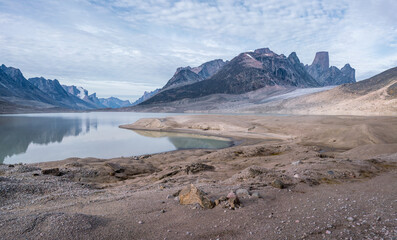 Fototapeta na wymiar Granite tower of Mt.Asgard and surrounding peaks reflect in waters of Glacier Lake in remote arctic valley of Akshayuk Pass, Baffin Island, Canada. Silent moment far in the wilderness of the north.