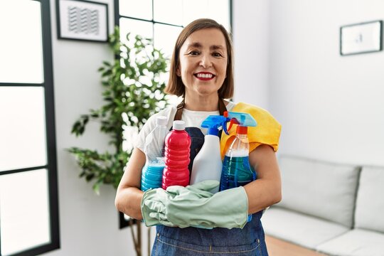 Middle age hispanic woman working as housekeeper holding products at home