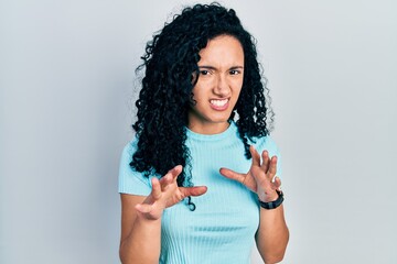 Young hispanic woman with curly hair wearing casual blue t shirt disgusted expression, displeased and fearful doing disgust face because aversion reaction. with hands raised